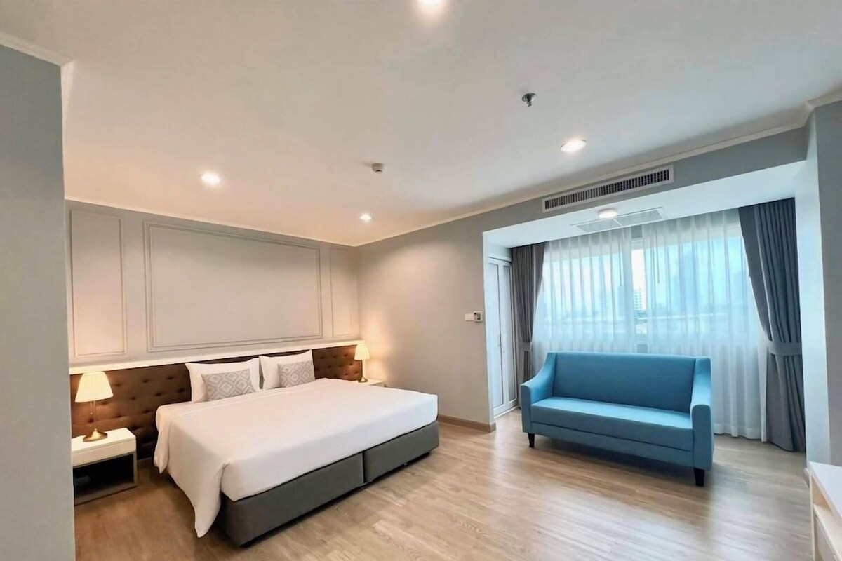 Ein modernes Hotelzimmer mit einem großen Bett, einer Sitzecke, einem Nachttisch und einem Fenster mit Vorhängen.