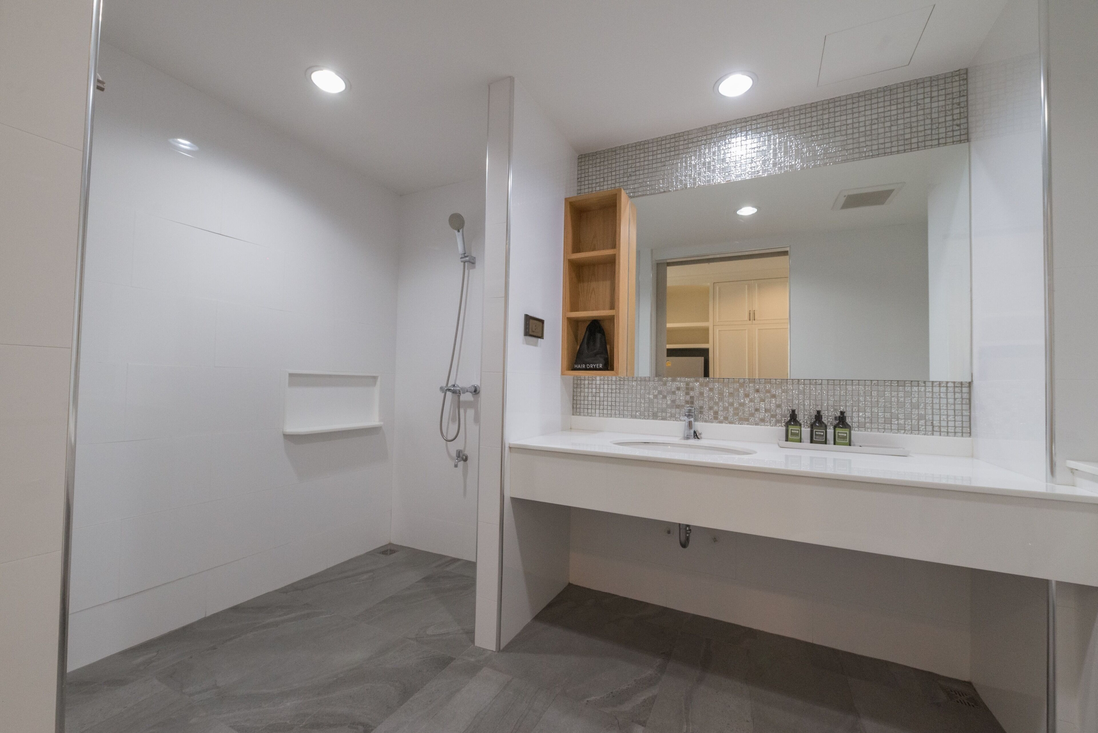 A modern bathroom with a walk-in shower, a large mirror, and a vanity with a sink and toiletries.