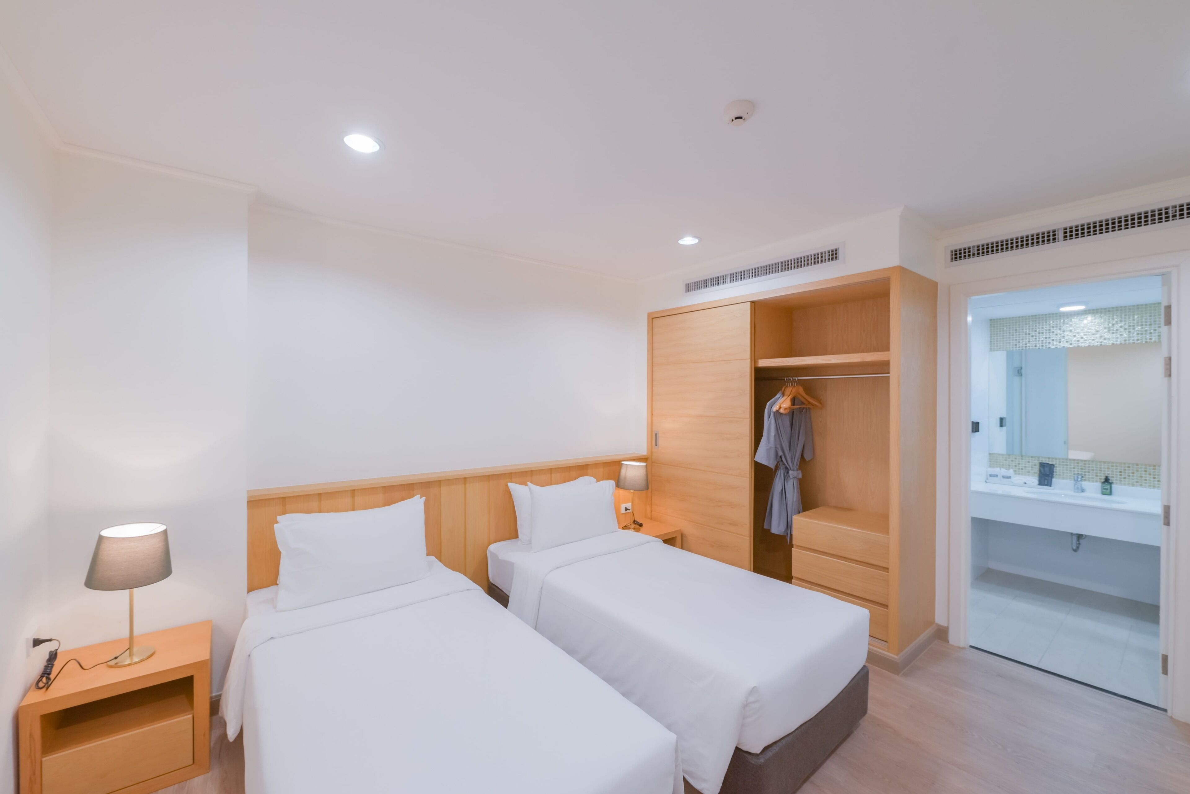 Habitación de hotel con dos camas, un armario, un espejo y baño con lavamanos y espejo.