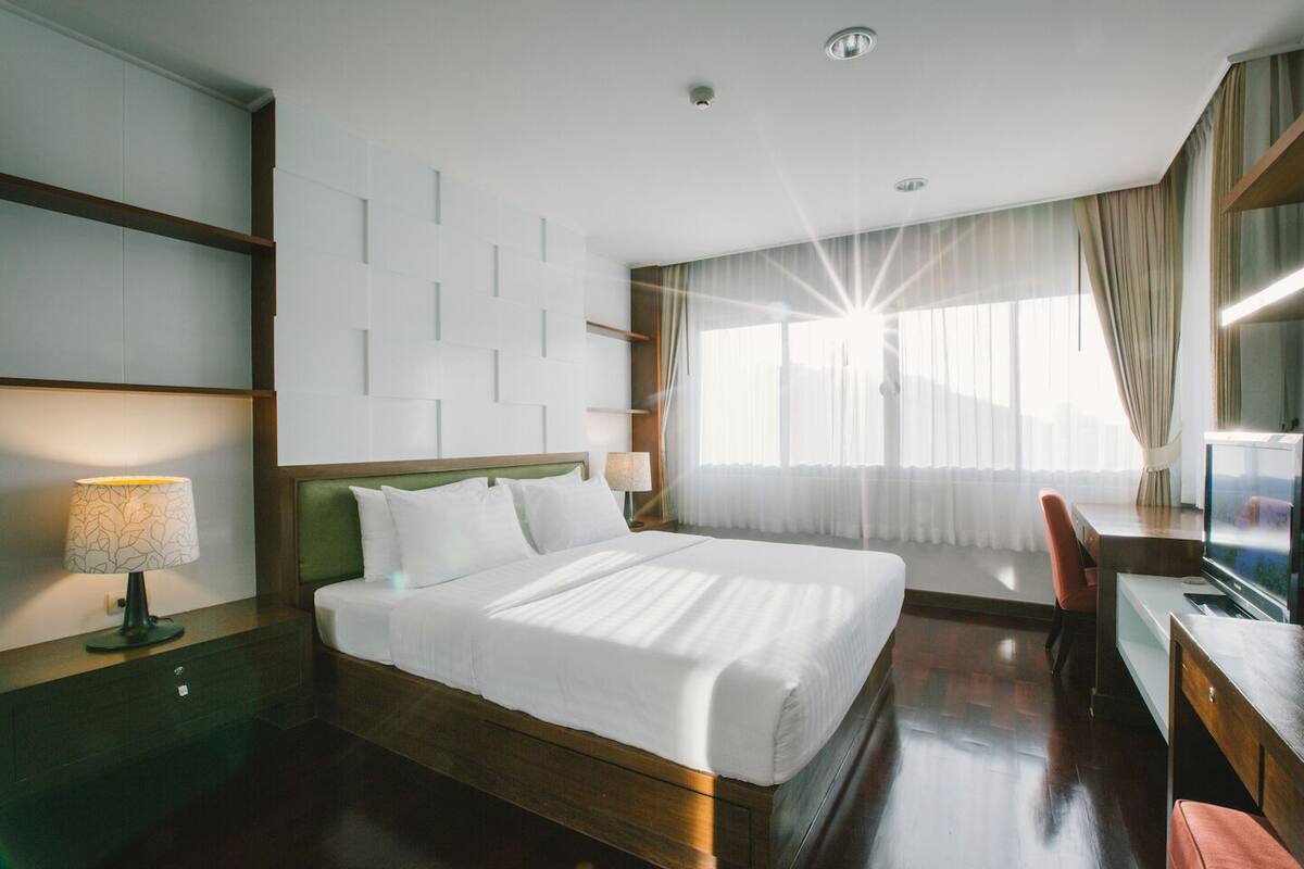 Habitación de hotel con cama, escritorio, silla, televisión y ventana con cortinas.