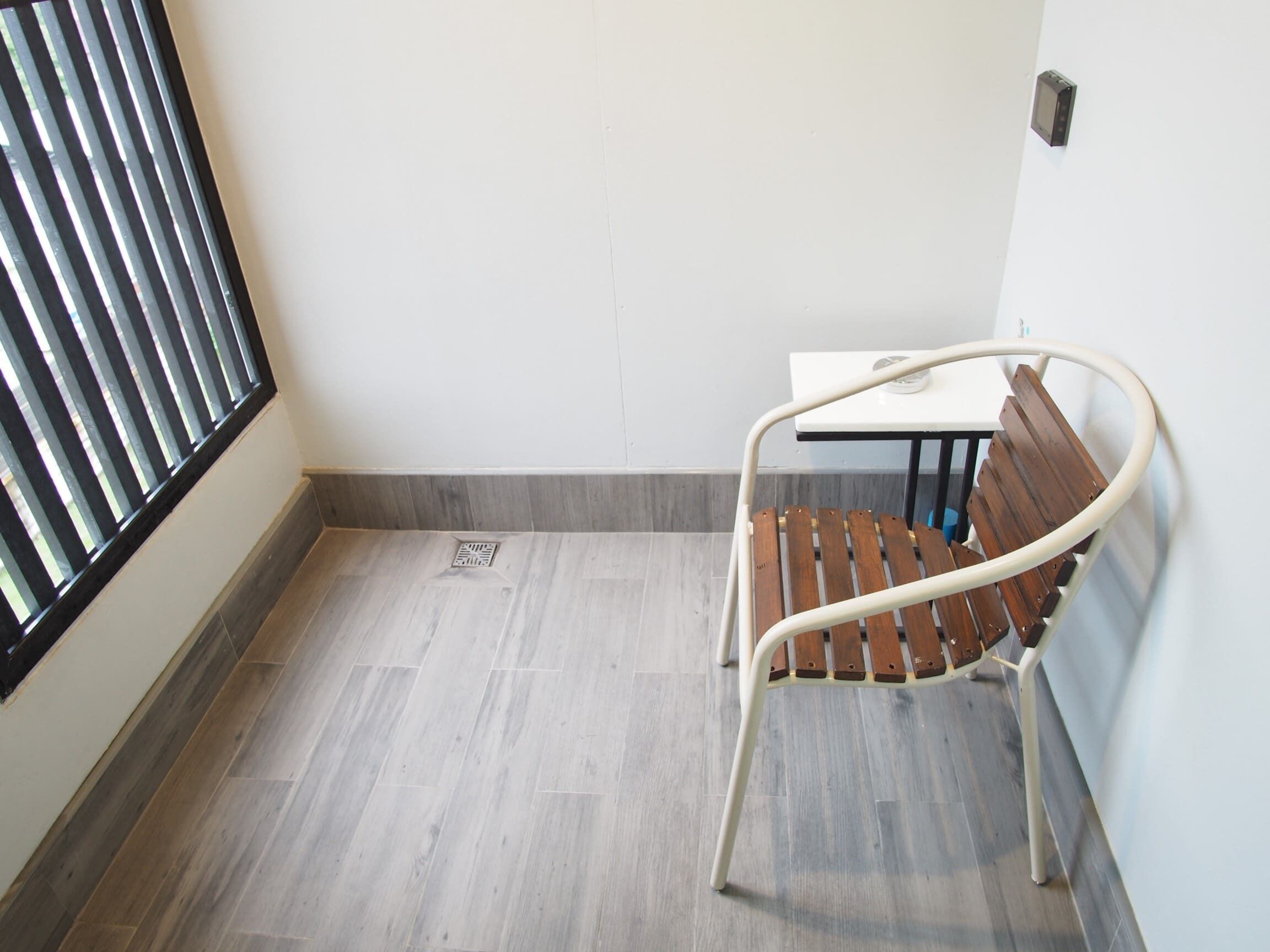 A corner room with a wooden bench, a small table, and a window with blinds.