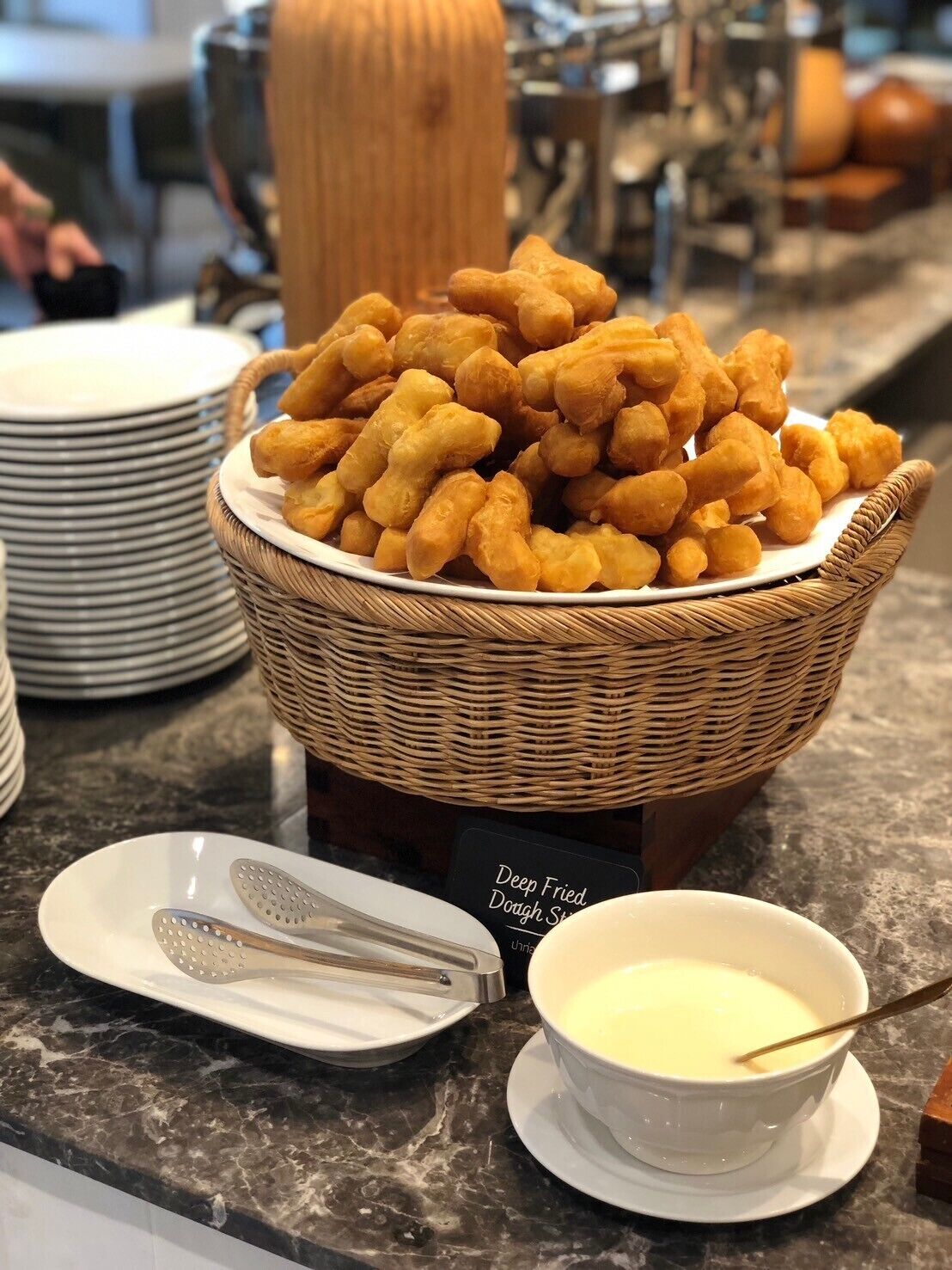 Una mesa de buffet con una cesta de churros, un recipiente con salsa para mojar y utensilios de servir.