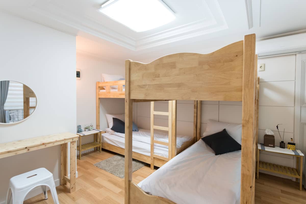 A room with bunk beds, a desk, a mirror, and a small stool.