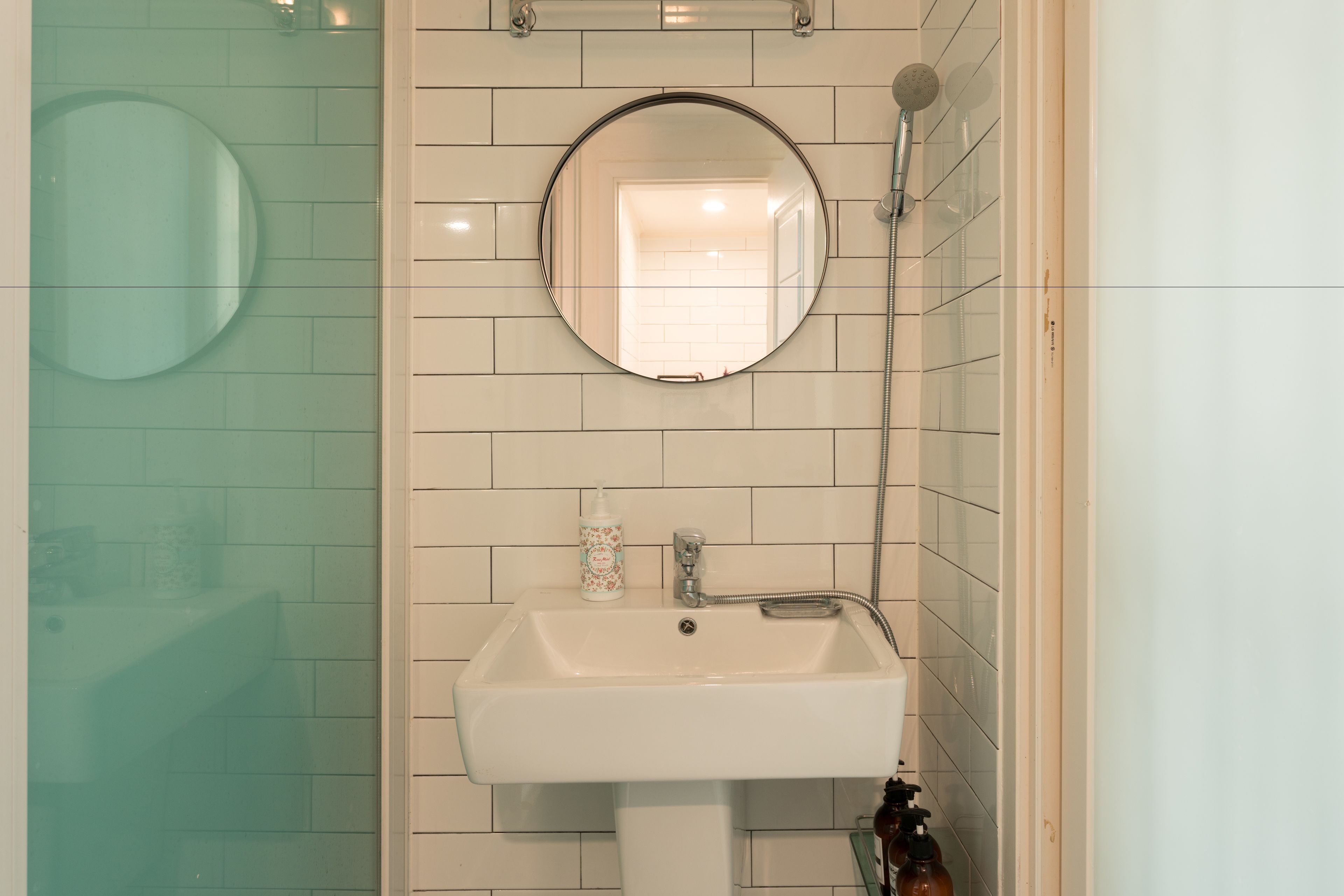 A bathroom with a white sink, a round mirror, and a shower.