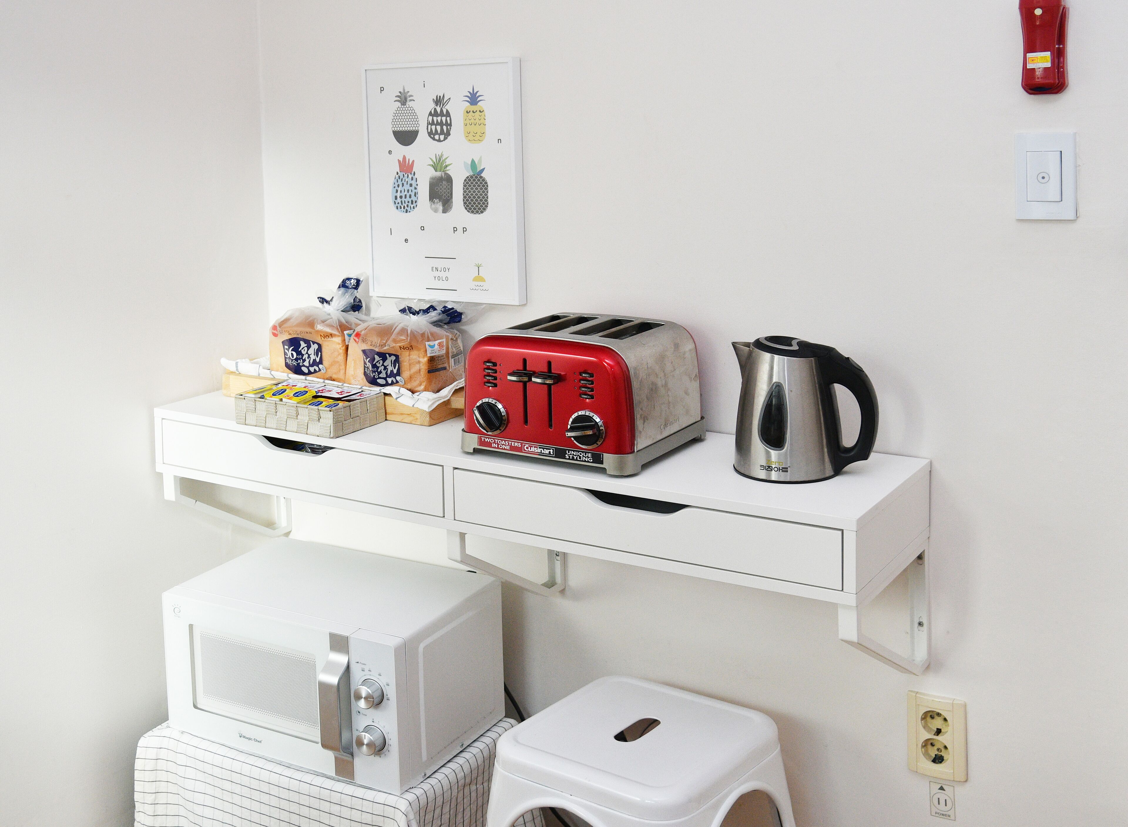 Una kitchenette con microondas blanco, tostadora, hervidor de agua y un pequeño taburete blanco.