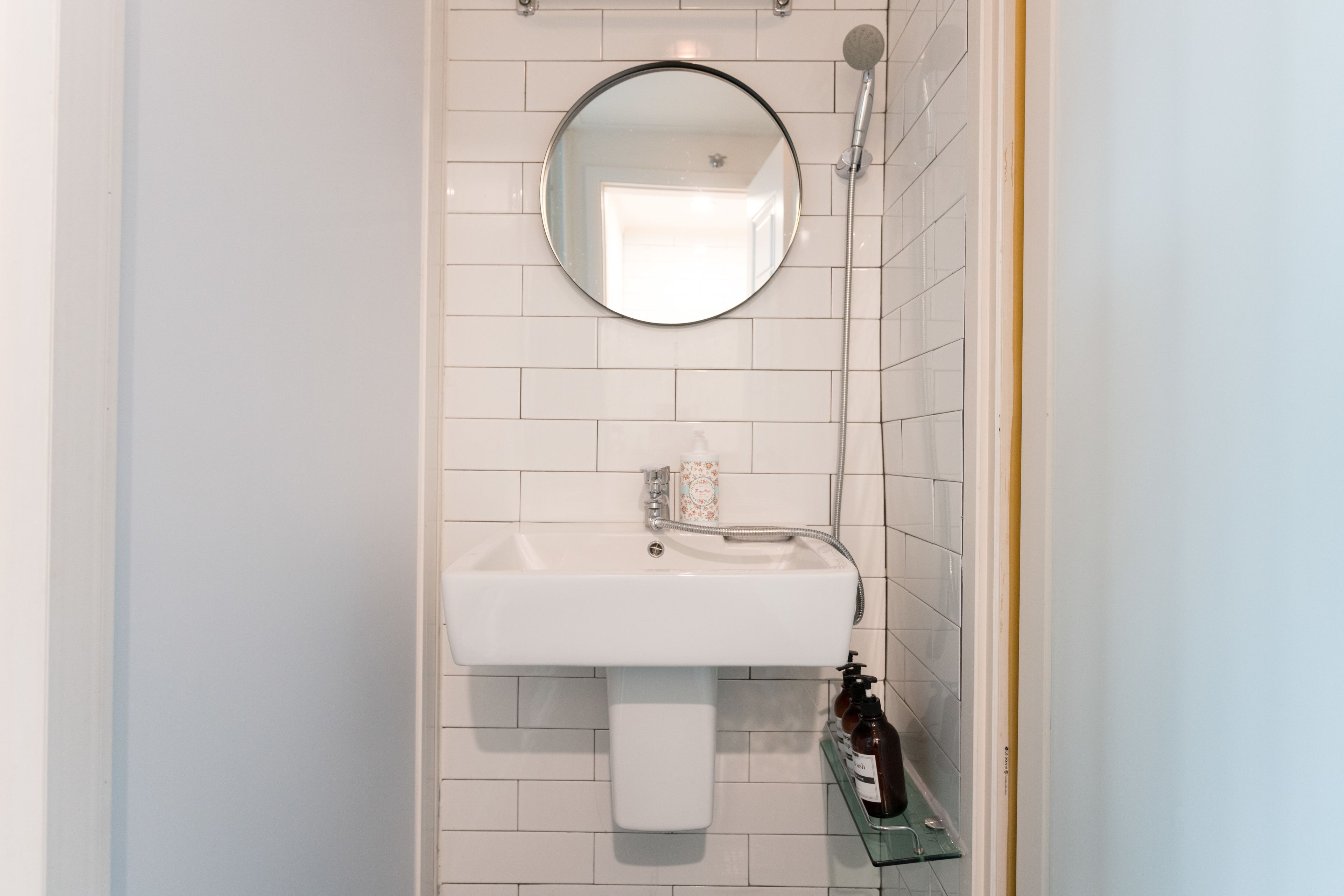 A bathroom with a white sink, a round mirror, and a glass shelf with toiletries.
