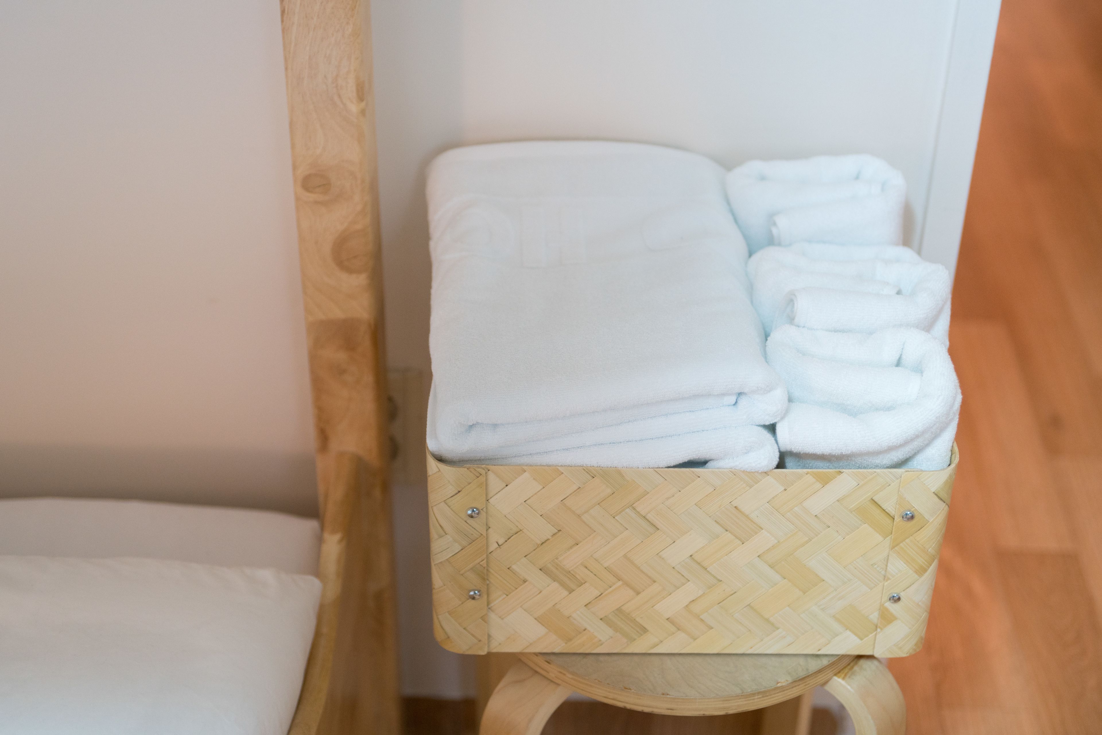 Un tabouret en bois avec un siège tissé et une boîte de rangement contenant des serviettes blanches pliées.