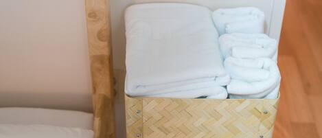 Un tabouret en bois avec un siège tissé et une boîte de rangement contenant des serviettes blanches pliées.