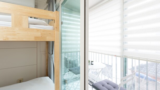 A room with a bunk bed, a glass door leading to a balcony with a table and chair, and a view of the cityscape. - The Blossom Yeonnam Guesthouse (Seoul)