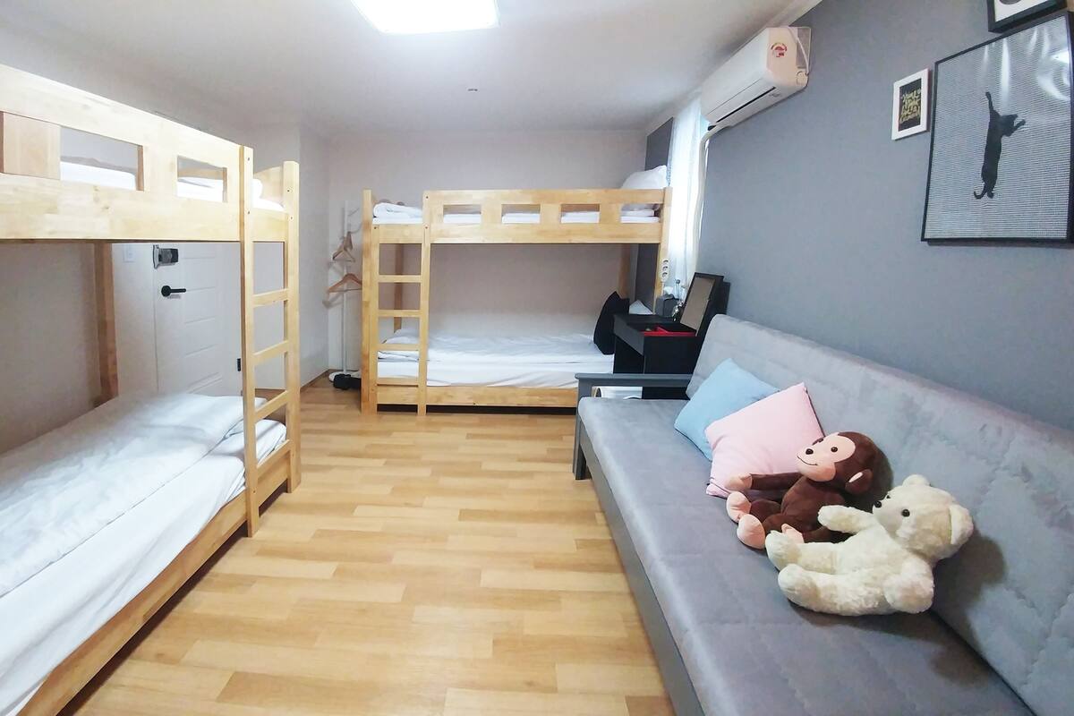 A dormitory room with bunk beds, a sofa, and a wall-mounted air conditioner.