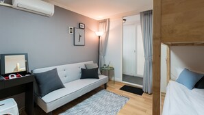 A modern hotel room with a sofa, a small table with a lamp, a bunk bed, and an air conditioning unit. - The Blossom Yeonnam Guesthouse (Seoul)