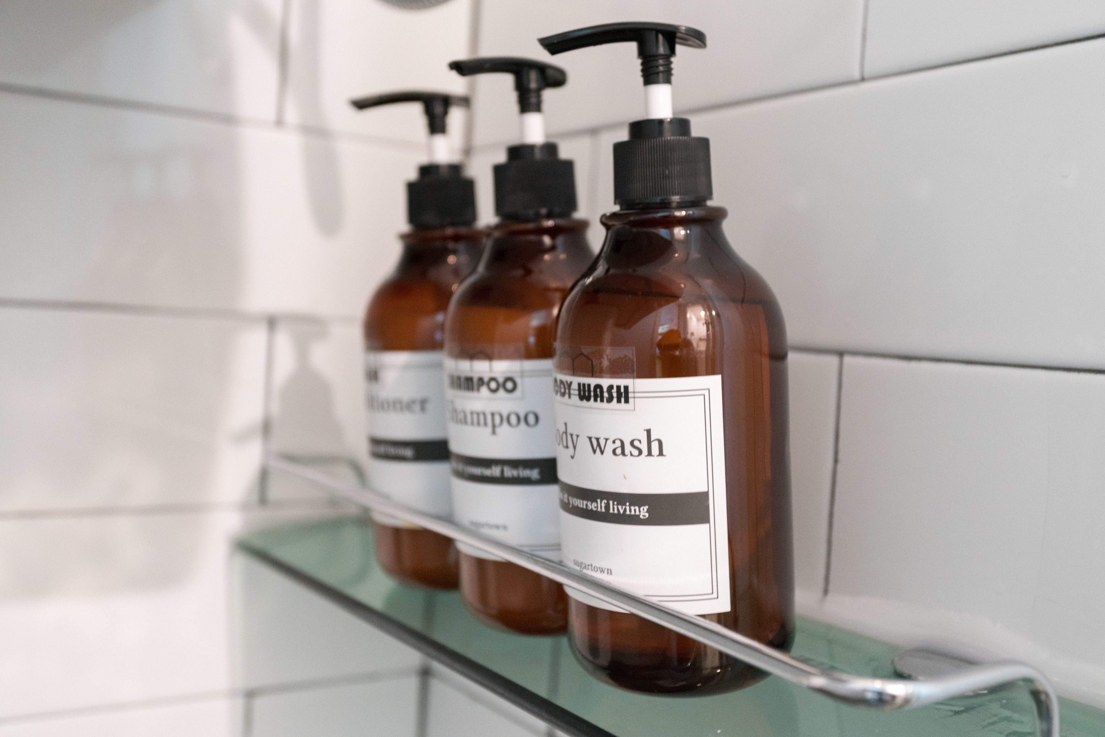 A row of brown bottles with black pumps on a glass shelf in a bathroom.