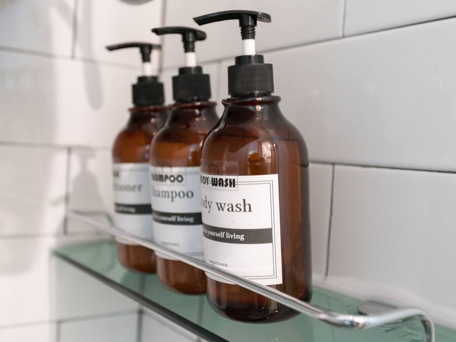 A row of brown bottles with black pumps on a glass shelf in a bathroom.