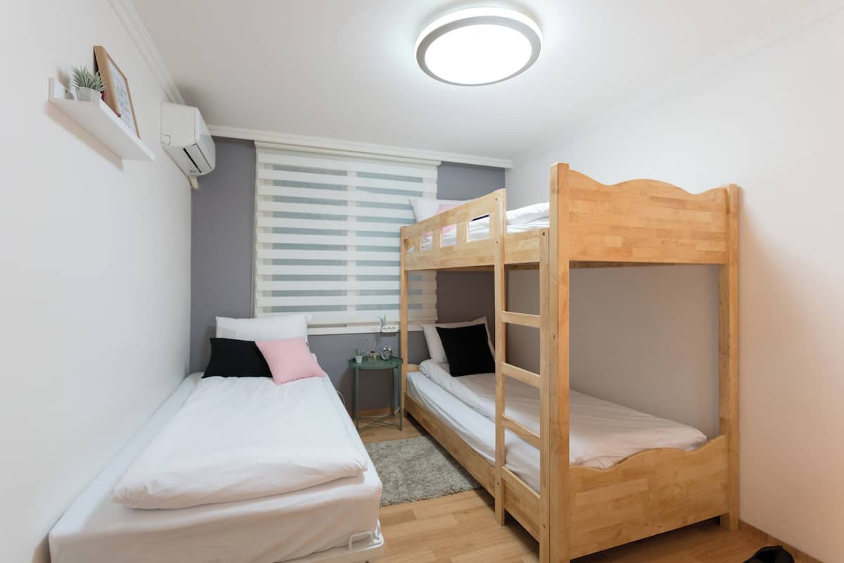 A small, well-lit room with two bunk beds, a small table, and a window with blinds.