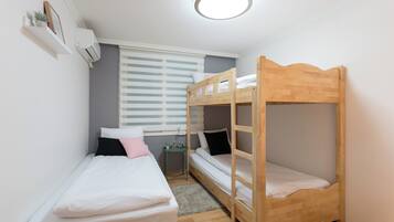 Una habitación pequeña y bien iluminada con dos literas, una mesita y una ventana con persianas.