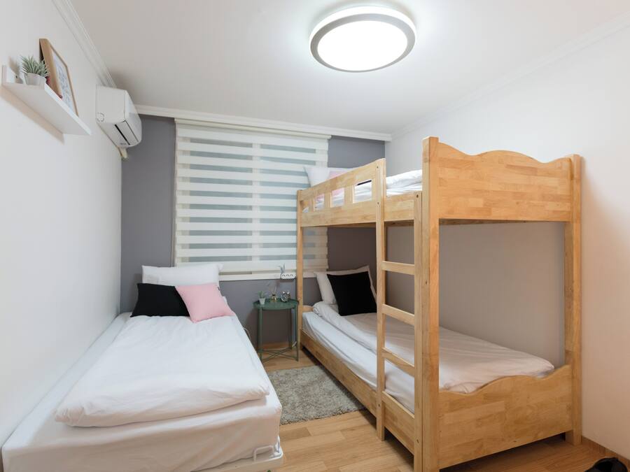 Una habitación pequeña y bien iluminada con dos literas, una mesita y una ventana con persianas.