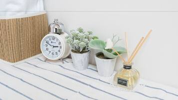 A bedside table with a striped cloth, a white analog alarm clock, two potted succulents, and a reed diffuser.