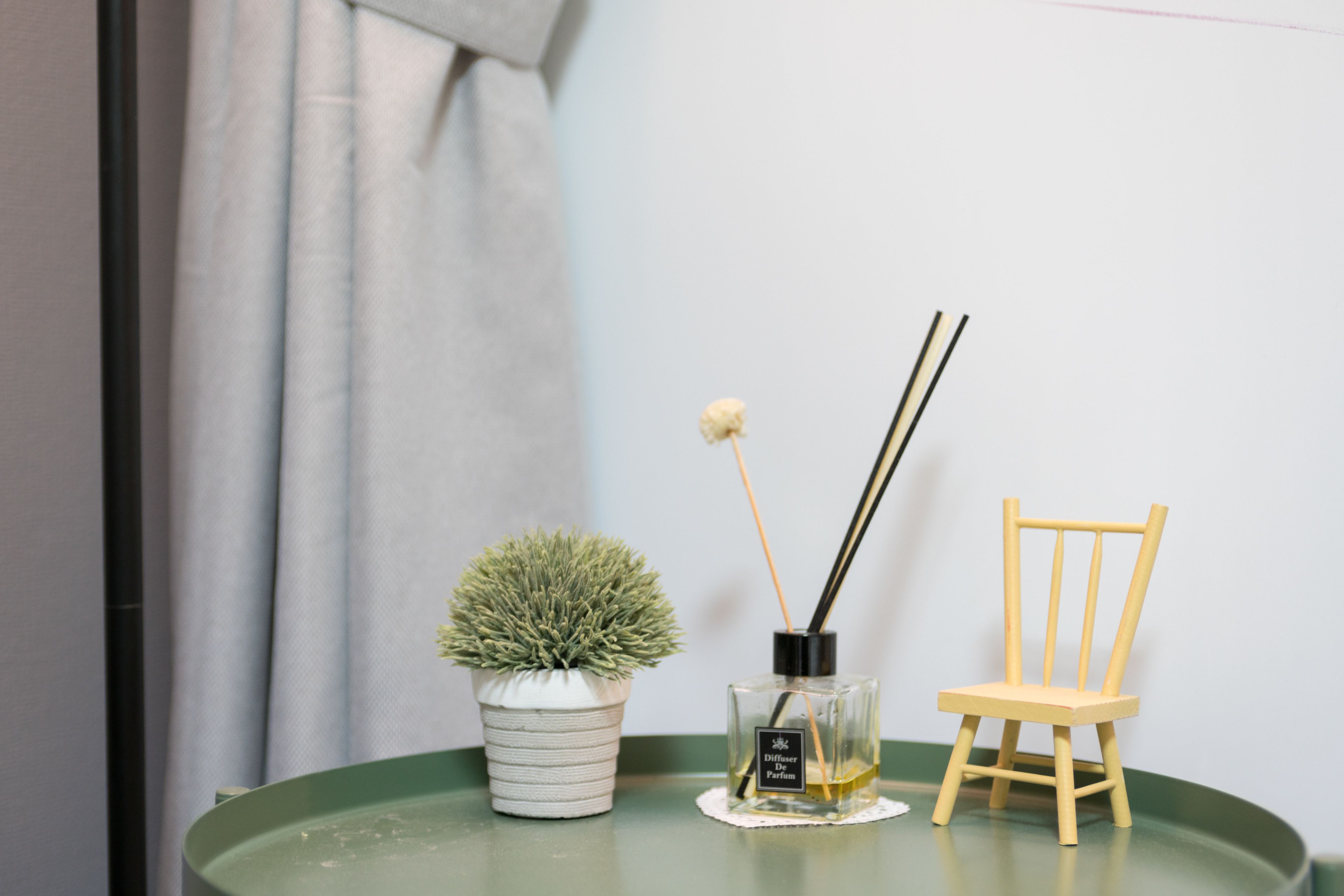 A small table with a potted plant, a perfume bottle, and a wooden chair.