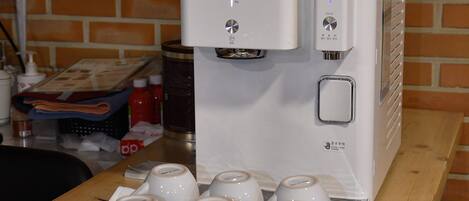 A coffee machine with a tray of white ceramic cups in front of it.