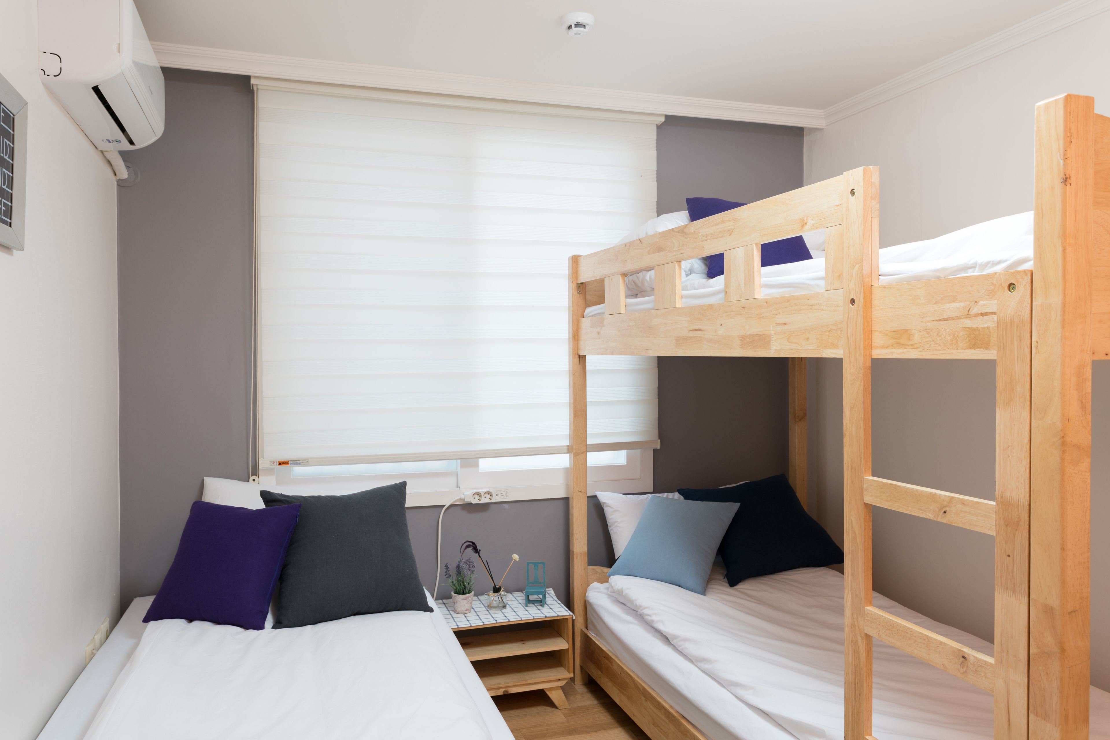 A bunk bed room with a window, a bedside table, and a wall-mounted air conditioner.