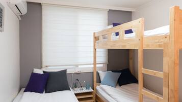 A bunk bed room with a window, a bedside table, and a wall-mounted air conditioner.
