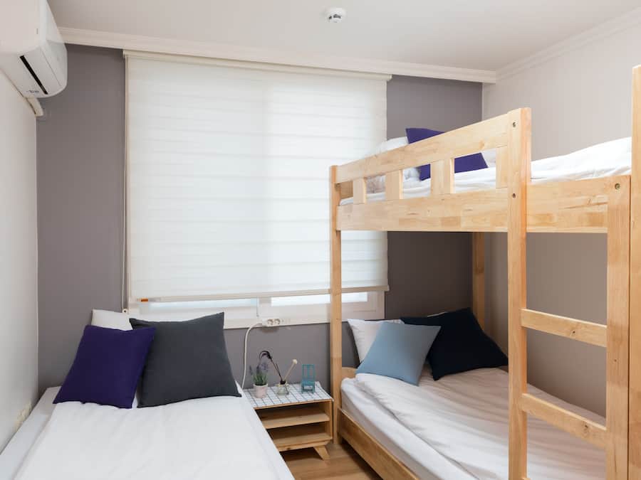 A bunk bed room with a window, a bedside table, and a wall-mounted air conditioner.
