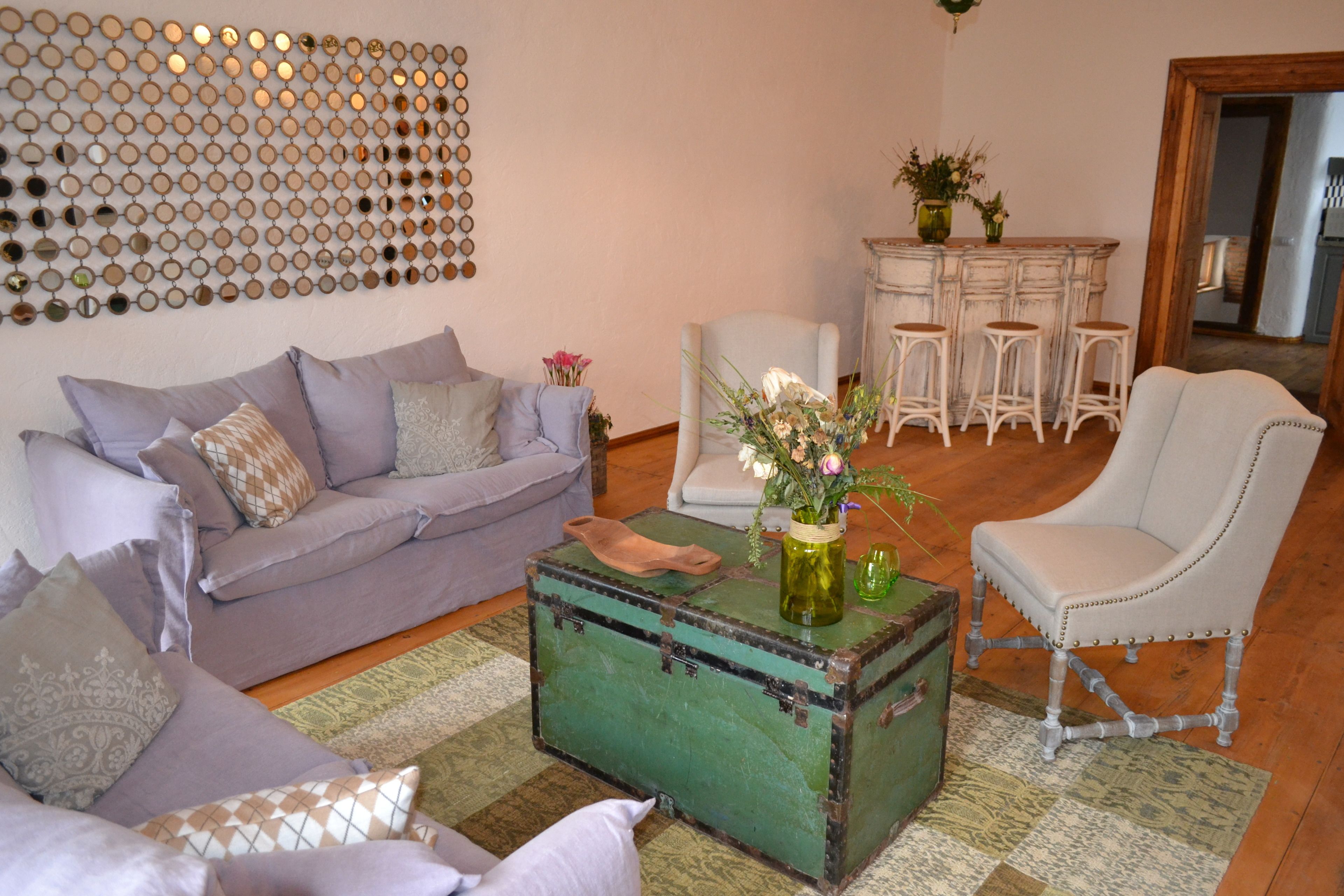 Een woonkamer met een groene koffer-salontafel, een grijze bank, een witte fauteuil en een bar met krukken.