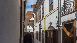 Uma viela estreita com calçamento de pedras, edifícios brancos com portas de madeira e um céu azul claro.