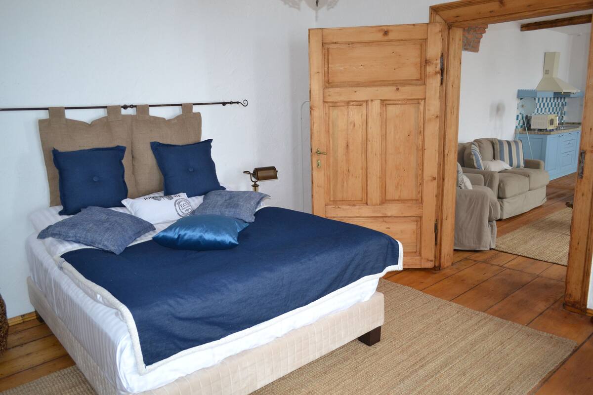 A bedroom with a bed, a wooden door, a kitchenette, and a seating area.