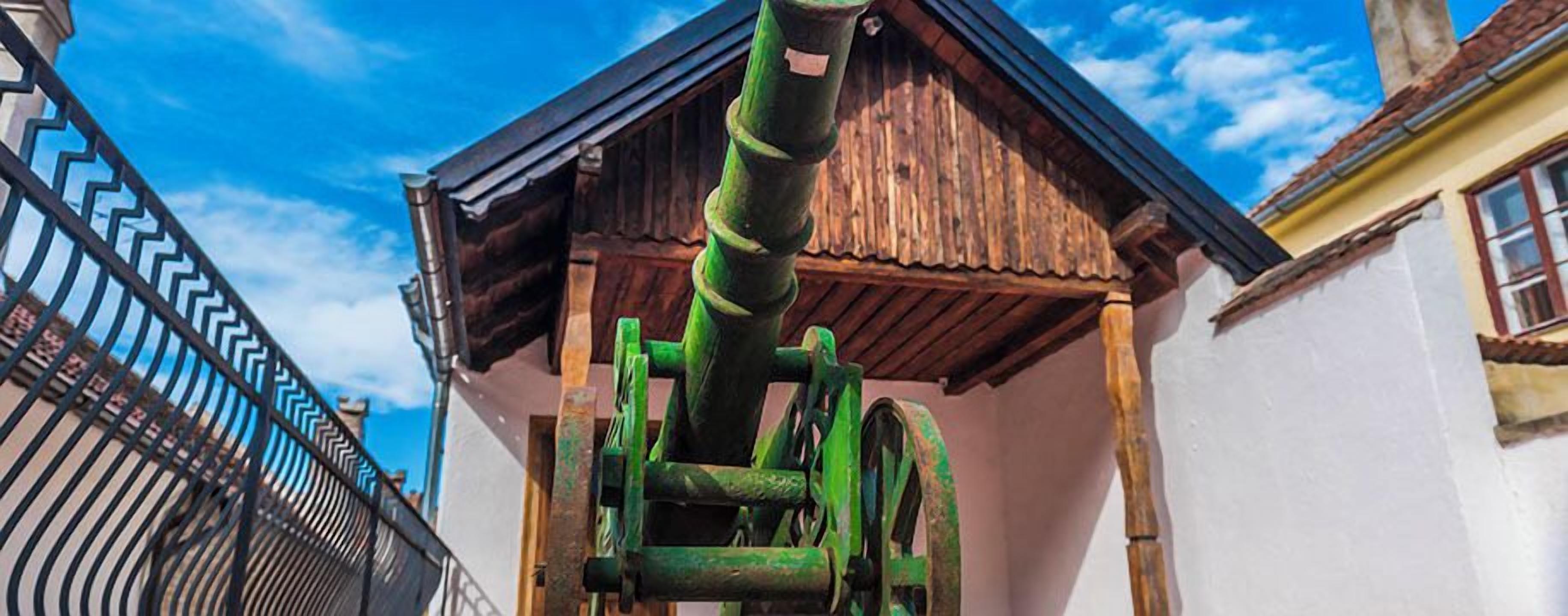 Ein traditionelles Holzgebäude mit einer grünen Metallkonstruktion davor.