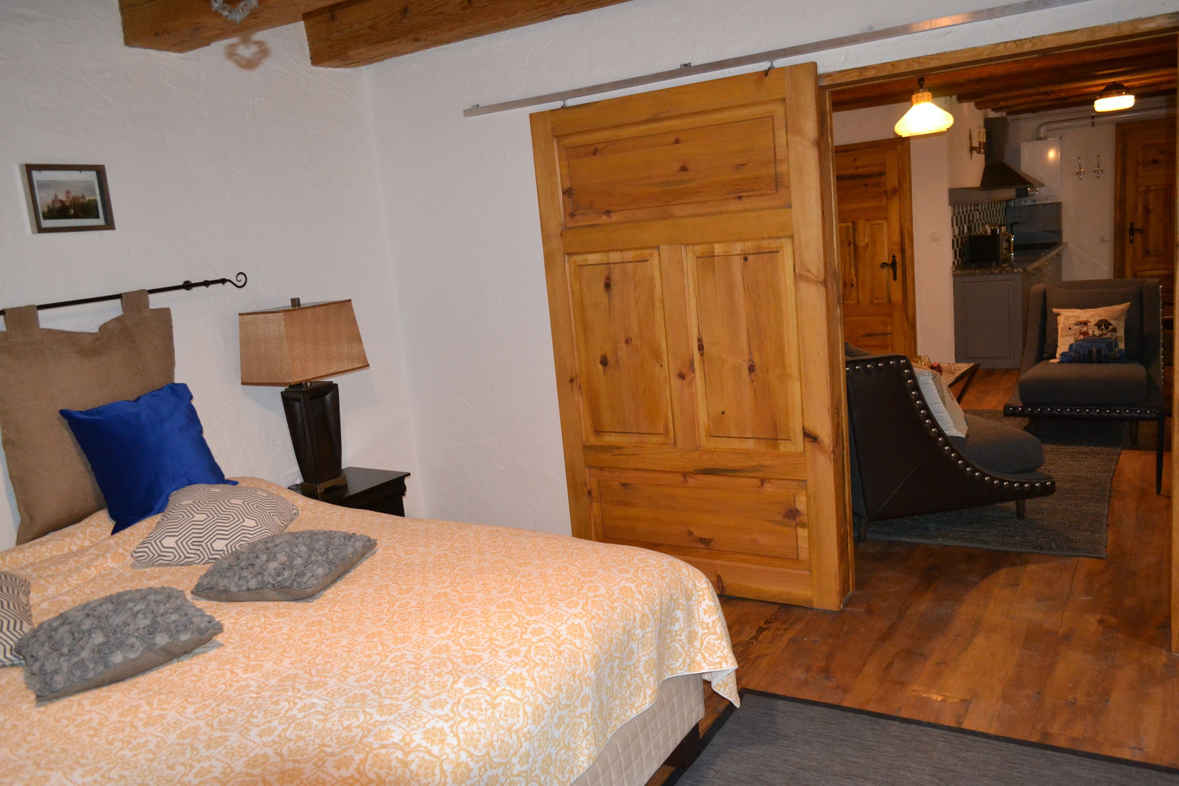 Un dormitorio con una cama, almohadas, una mesita de noche, un armario de madera y una silla.