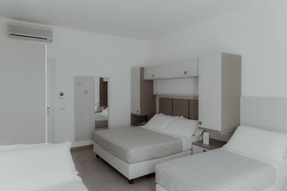 A modern hotel room with two beds, a wardrobe, a bedside table, and a mirror.