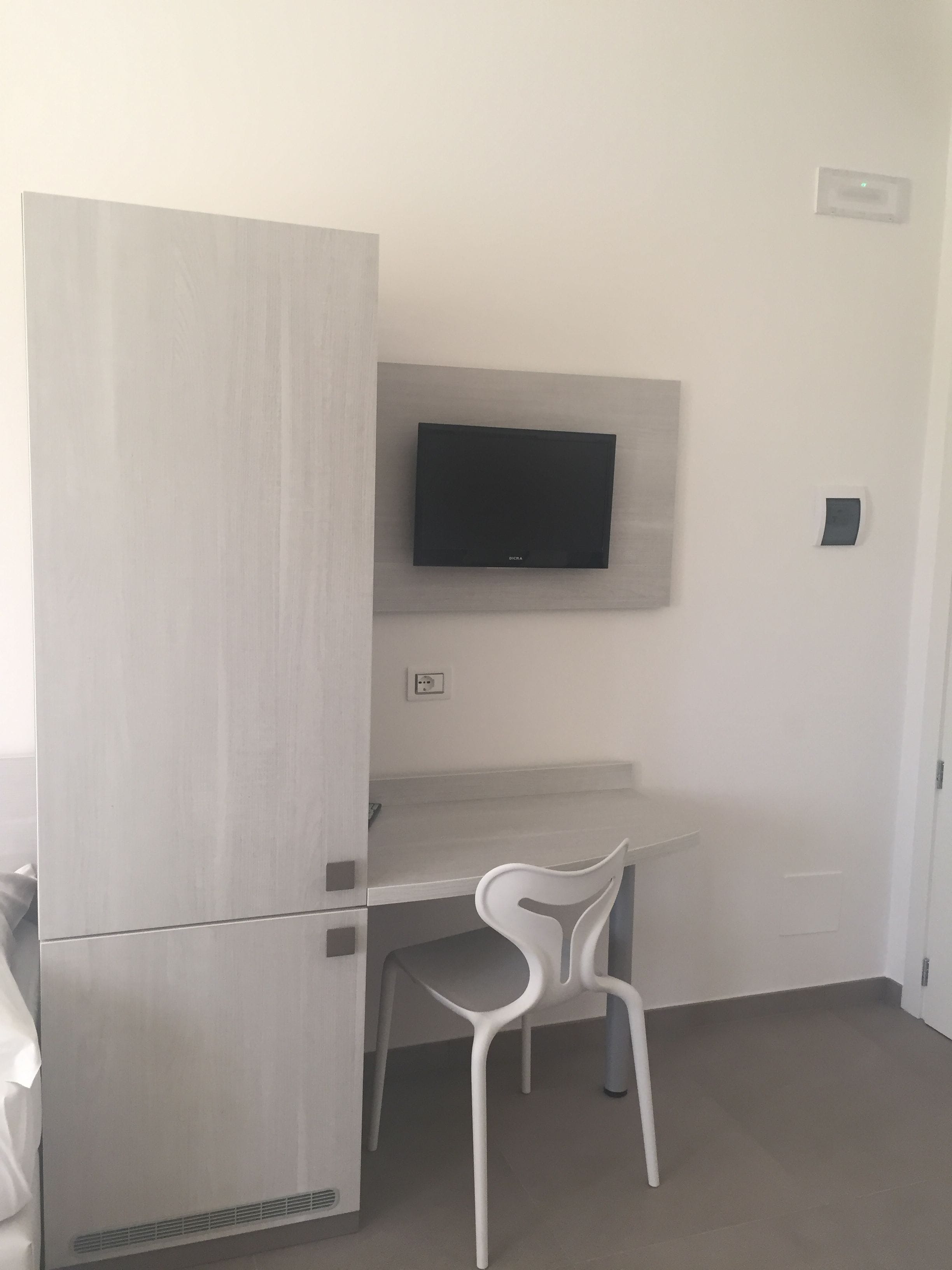 Une pièce compacte équipée d’un réfrigérateur intégré, d’un téléviseur à écran plat fixé au mur et d’une chaise blanche.
