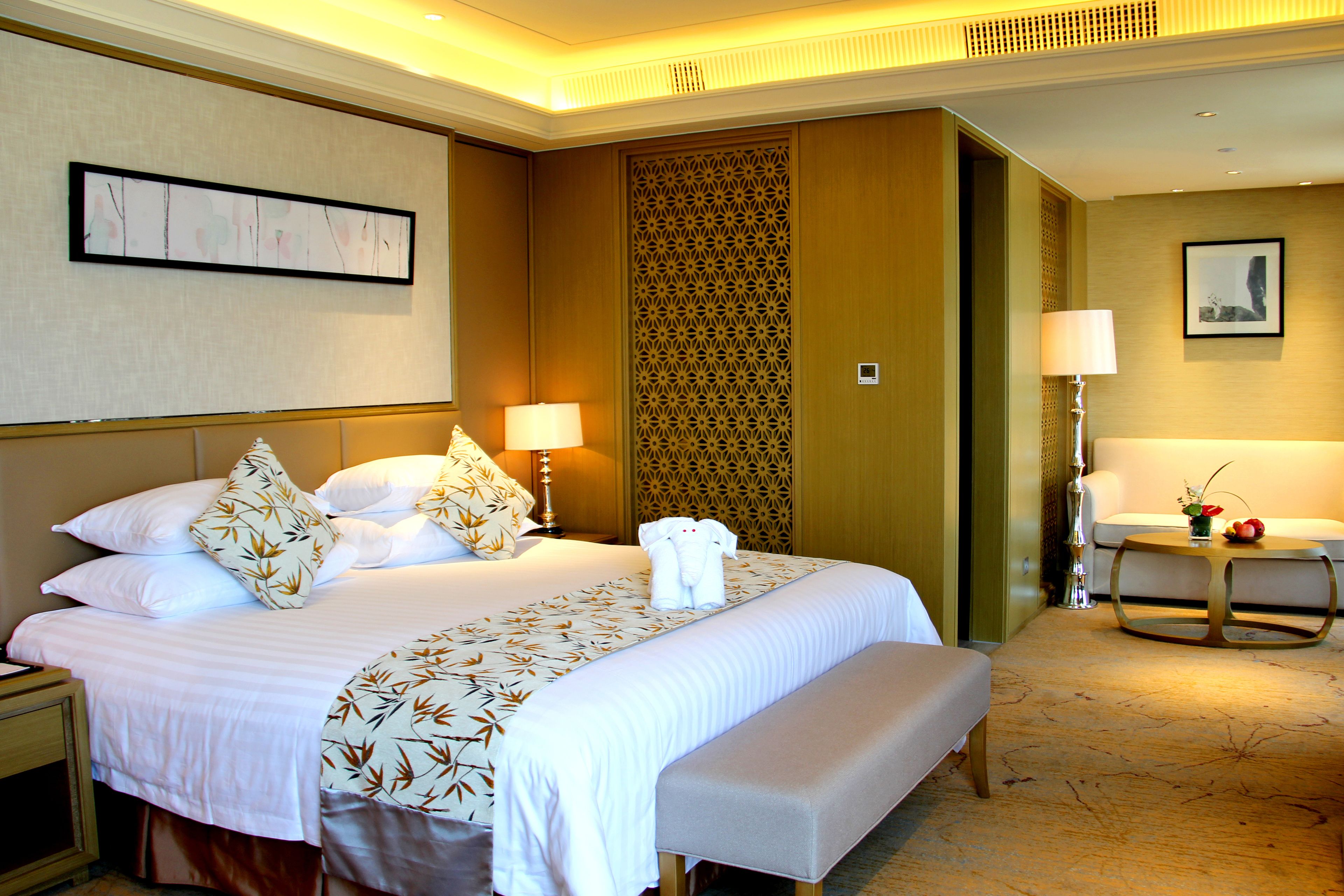 A hotel room with a large bed, a bench, a desk, and a chair.