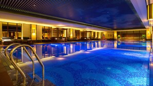 Una amplia piscina interior con suelo iluminado en azul, rodeada por una zona de recepción con asientos y un bar.