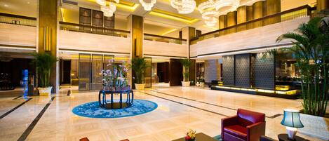 A spacious lobby with a central floral arrangement, multiple seating areas, and a high ceiling with chandeliers.