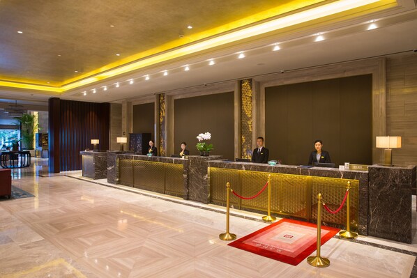 A hotel reception area with marble counters, a red carpet, and gold stanchions. - Grand New Century Hotel Yuhang Hangzhou (Hangzhou)