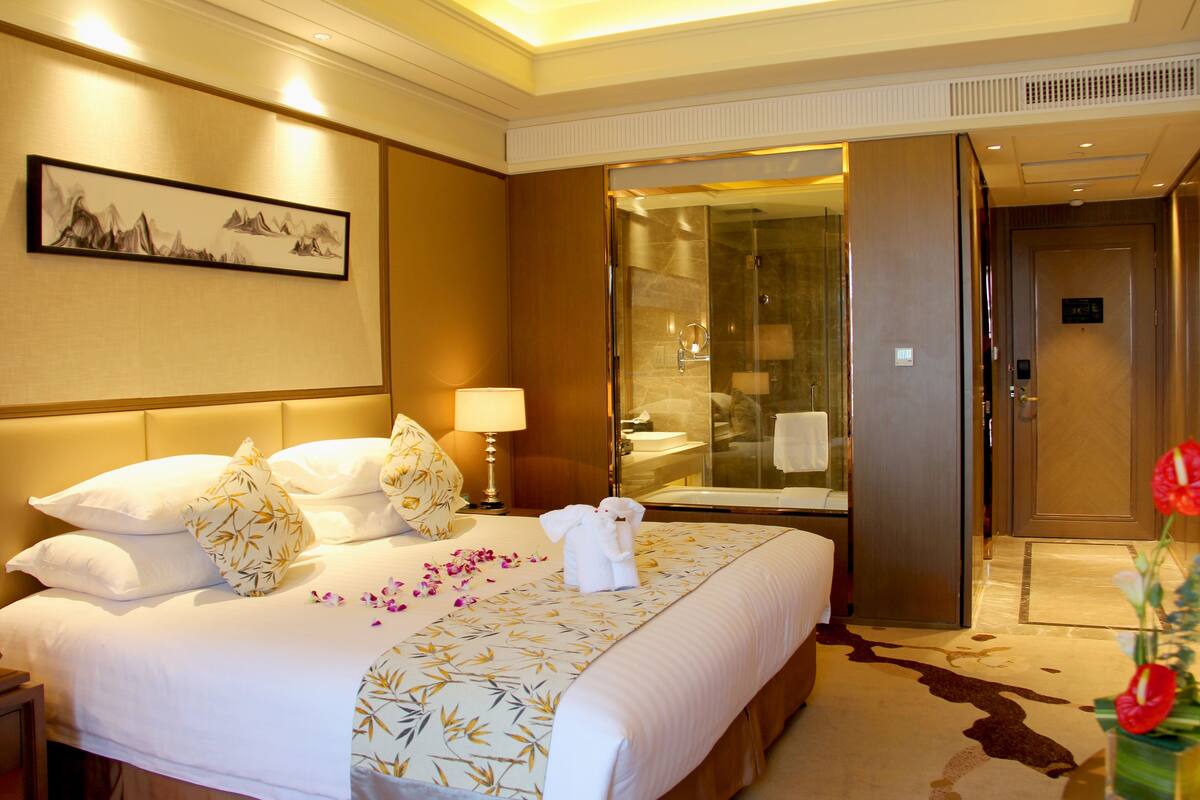Ein Hotelzimmer mit einem großen Bett, einem Badezimmer mit Glasdusche und einer Tür zu einem weiteren Raum.