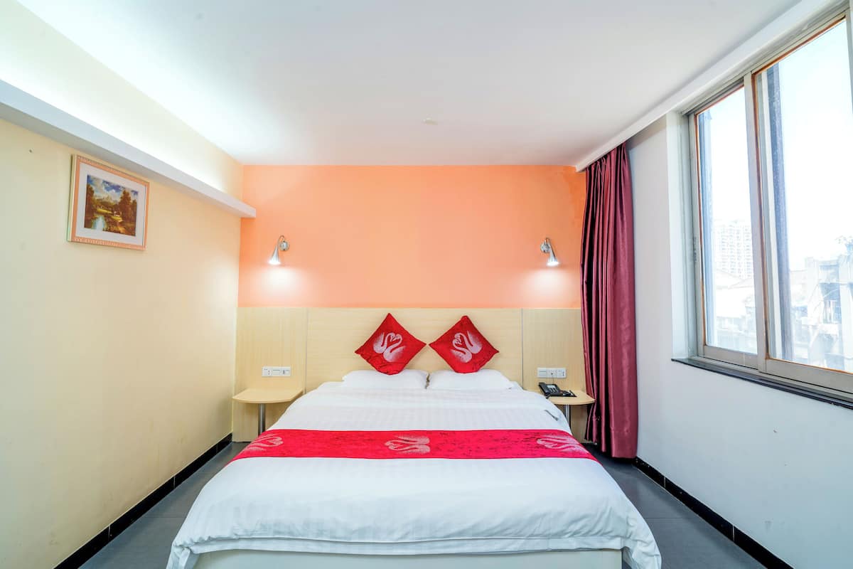 Une chambre d’hôtel comprenant un lit, une table de chevet, une lampe, une fenêtre avec des rideaux et un tableau accroché au mur.