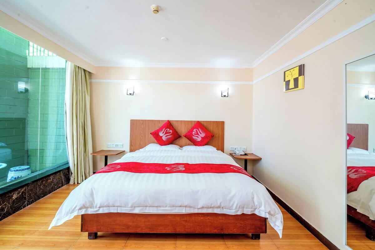 Une chambre d’hôtel avec un grand lit, une tête de lit en bois, deux tables de chevet et un miroir au mur.
