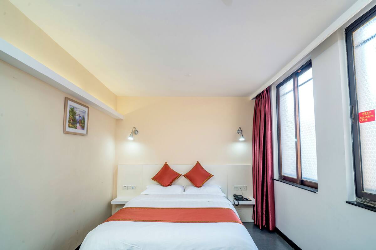Une chambre d’hôtel avec un lit, une table de chevet, un téléphone et une fenêtre avec des rideaux.