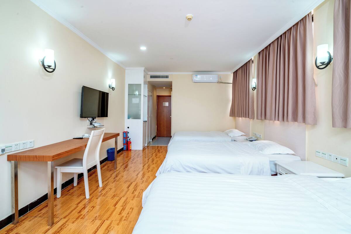 Une chambre d’hôtel avec deux lits, un bureau avec une chaise, une télévision et une porte de salle de bain.