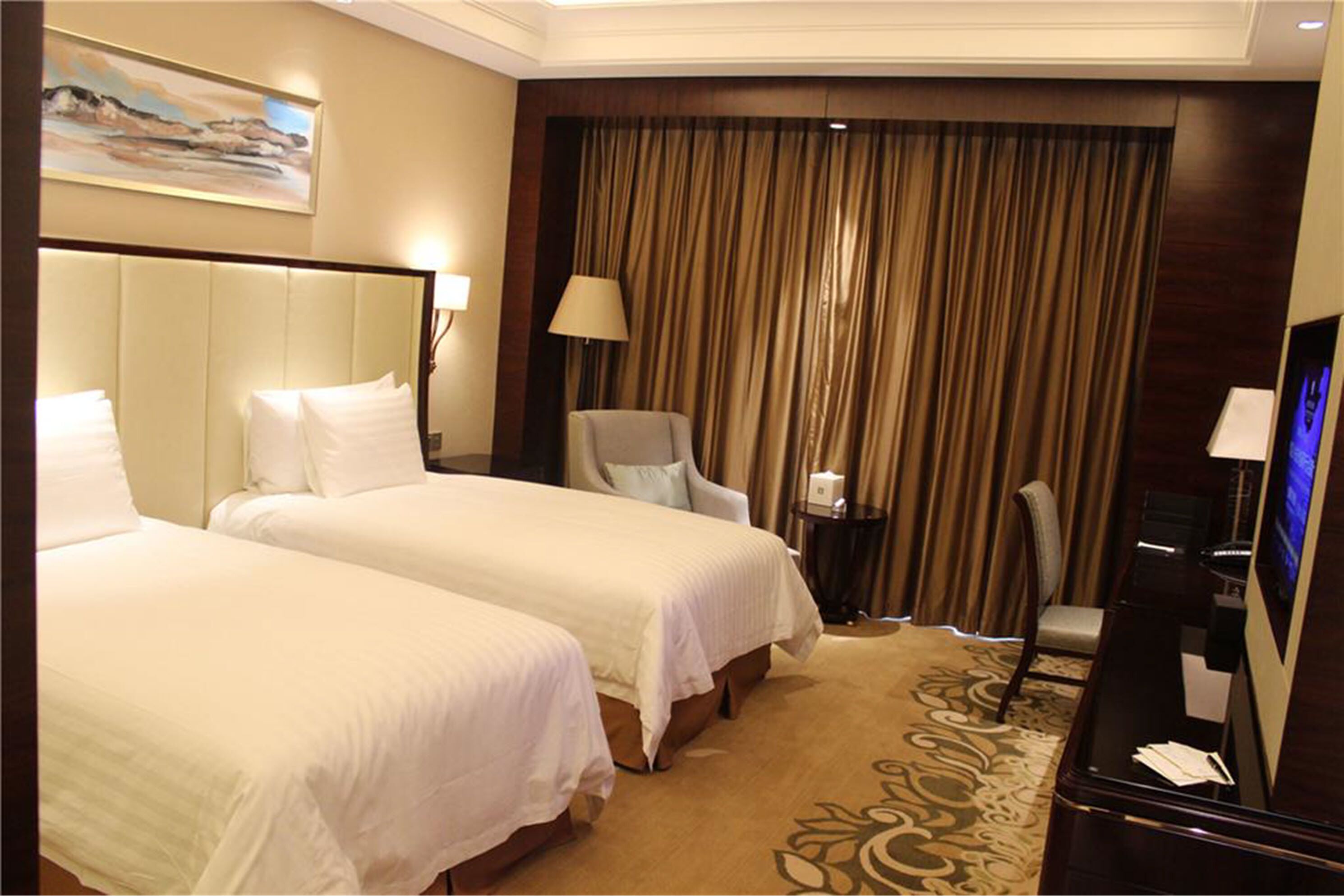 A hotel room with two beds, a desk, a chair, a TV, and a curtain backdrop.