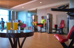 A gym area with exercise equipment, a table with drinks and a flower, and a person in the background.