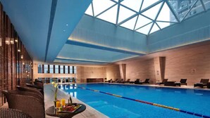 Una piscina interior con sillones de descanso y una mesa con fruta y bebidas.