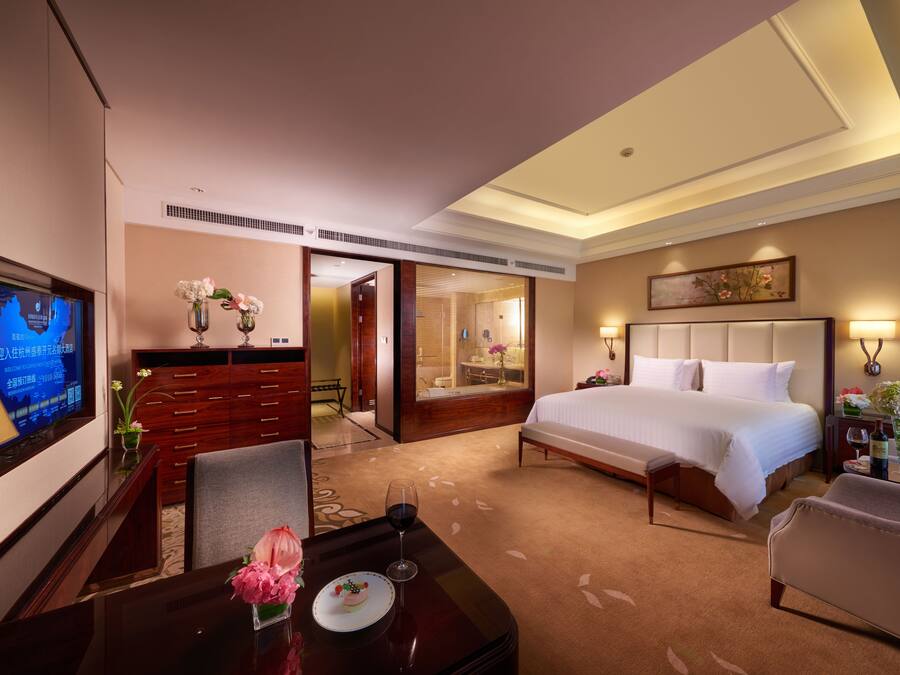 A hotel room with a bed, a desk with a computer, a TV, and a bathroom visible through an open door.