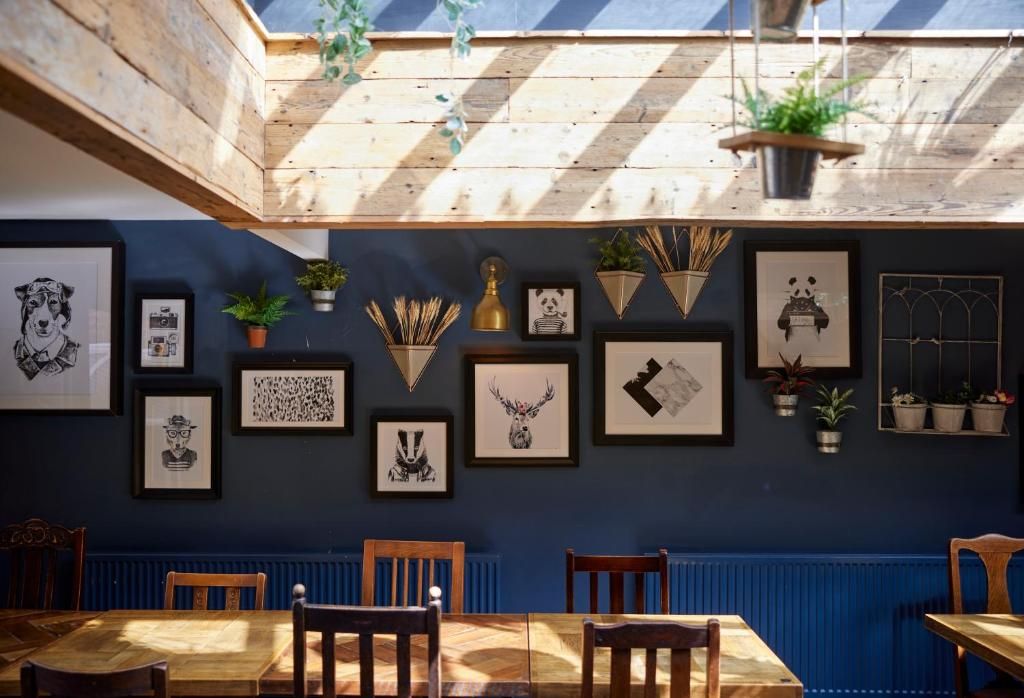 Un comedor con mesa y sillas de madera, una pared azul decorada con cuadros, y un tragaluz arriba.