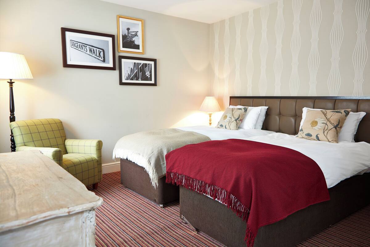 A hotel room with a bed, a chair, a lamp, and framed pictures on the wall.
