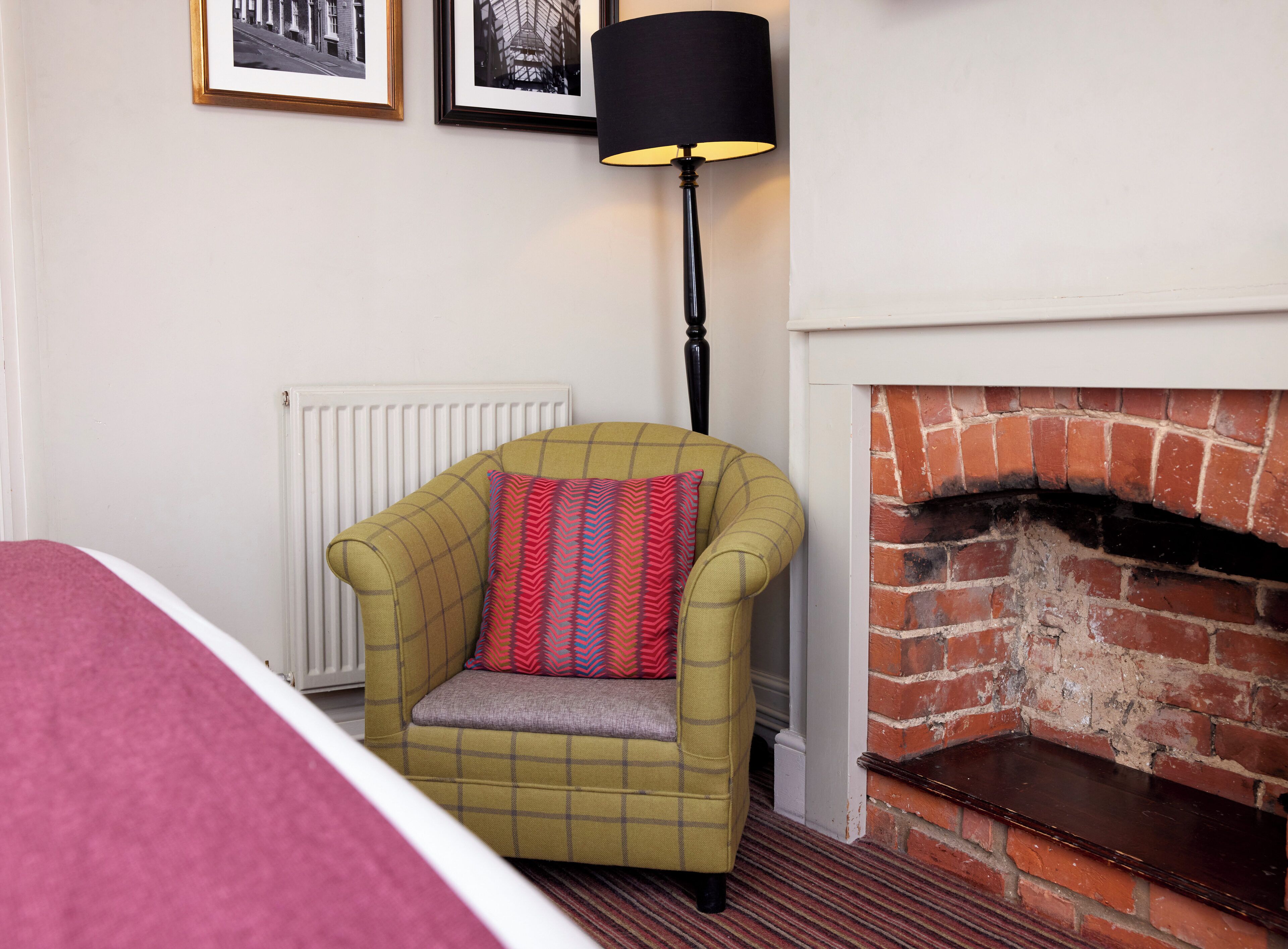 Una habitación con un sillón a cuadros, una chimenea y dos cuadros enmarcados en la pared.