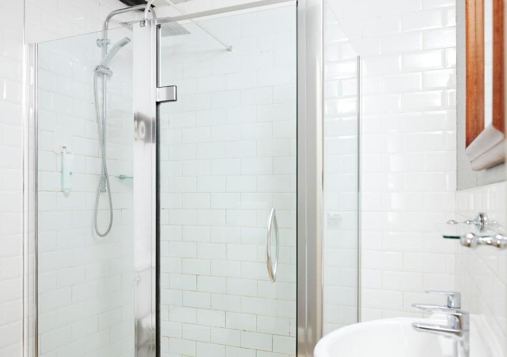 A bathroom with a glass-enclosed shower, white tiled walls, and a white sink with chrome fixtures.